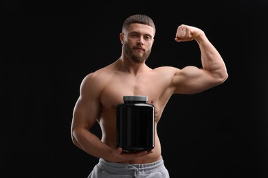 Young man with muscular body holding jar of protein powder on black background