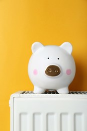 Photo of Piggy bank on heating radiator against orange background