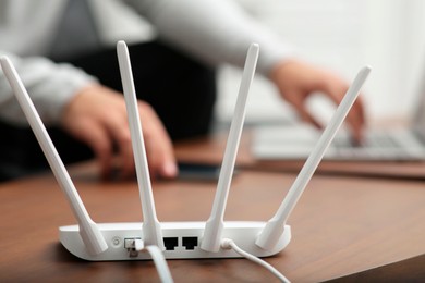 Photo of Man with laptop and smartphone working at wooden table, focus on Wi-Fi router