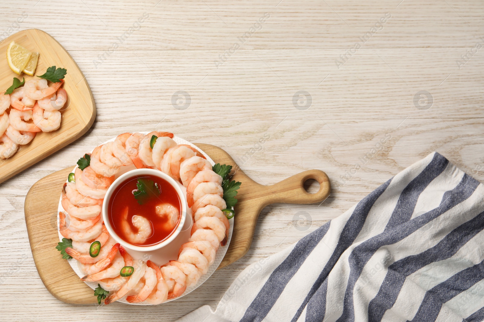 Photo of Tasty boiled shrimps with cocktail sauce, chili and parsley on light wooden table, top view. Space for text