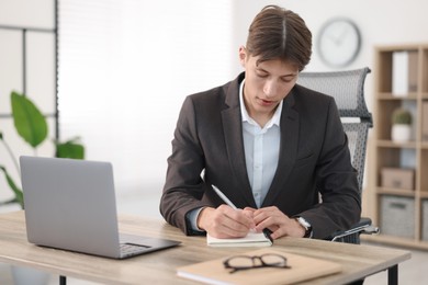 Photo of Man taking notes during webinar at wooden table indoors