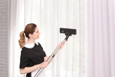 Photo of Female worker removing dust from curtains with professional vacuum cleaner indoors