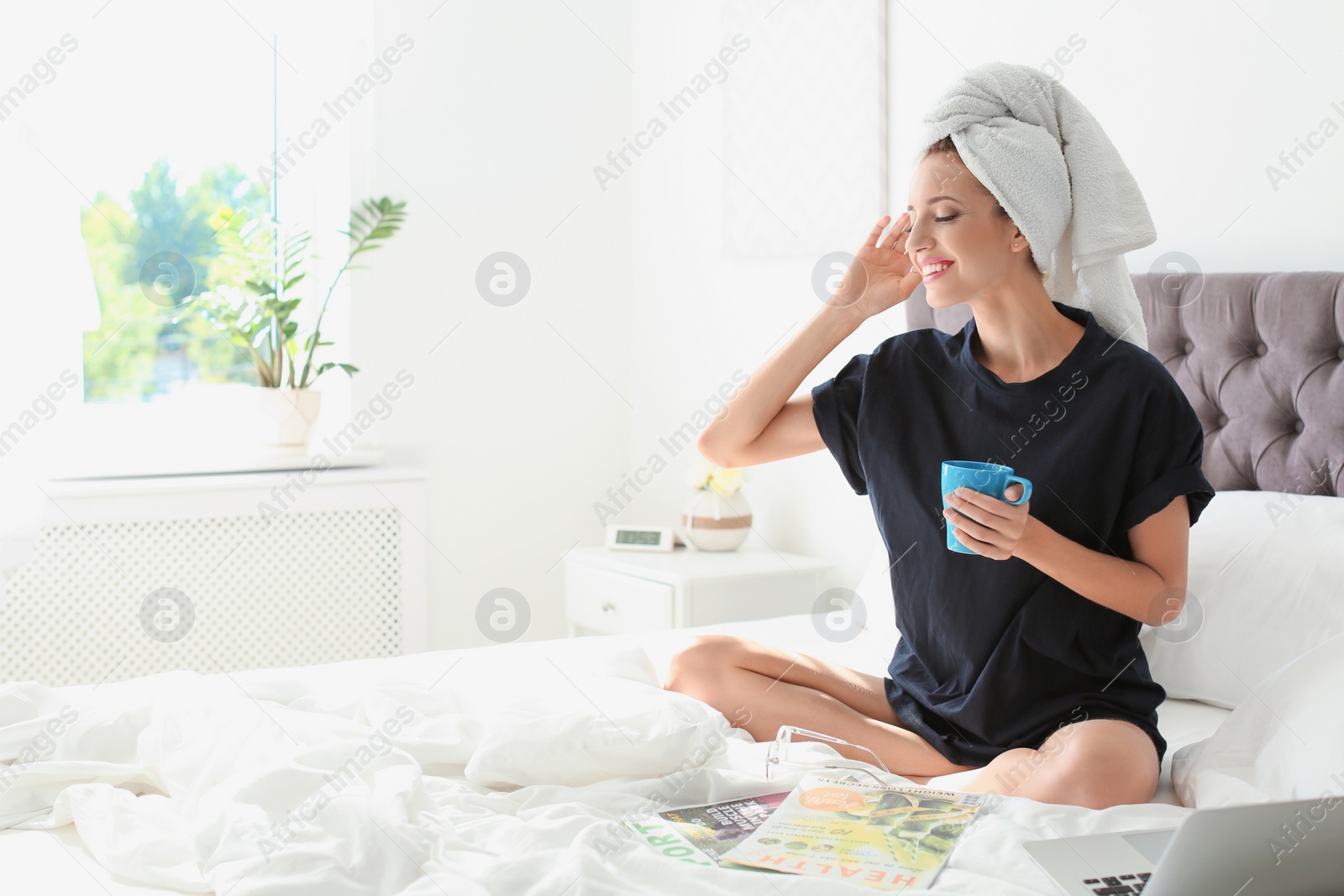 Photo of Beautiful young woman with cup of coffee sitting in bed at home. Lazy morning