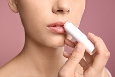 Young woman applying balm on her lips against color background, closeup