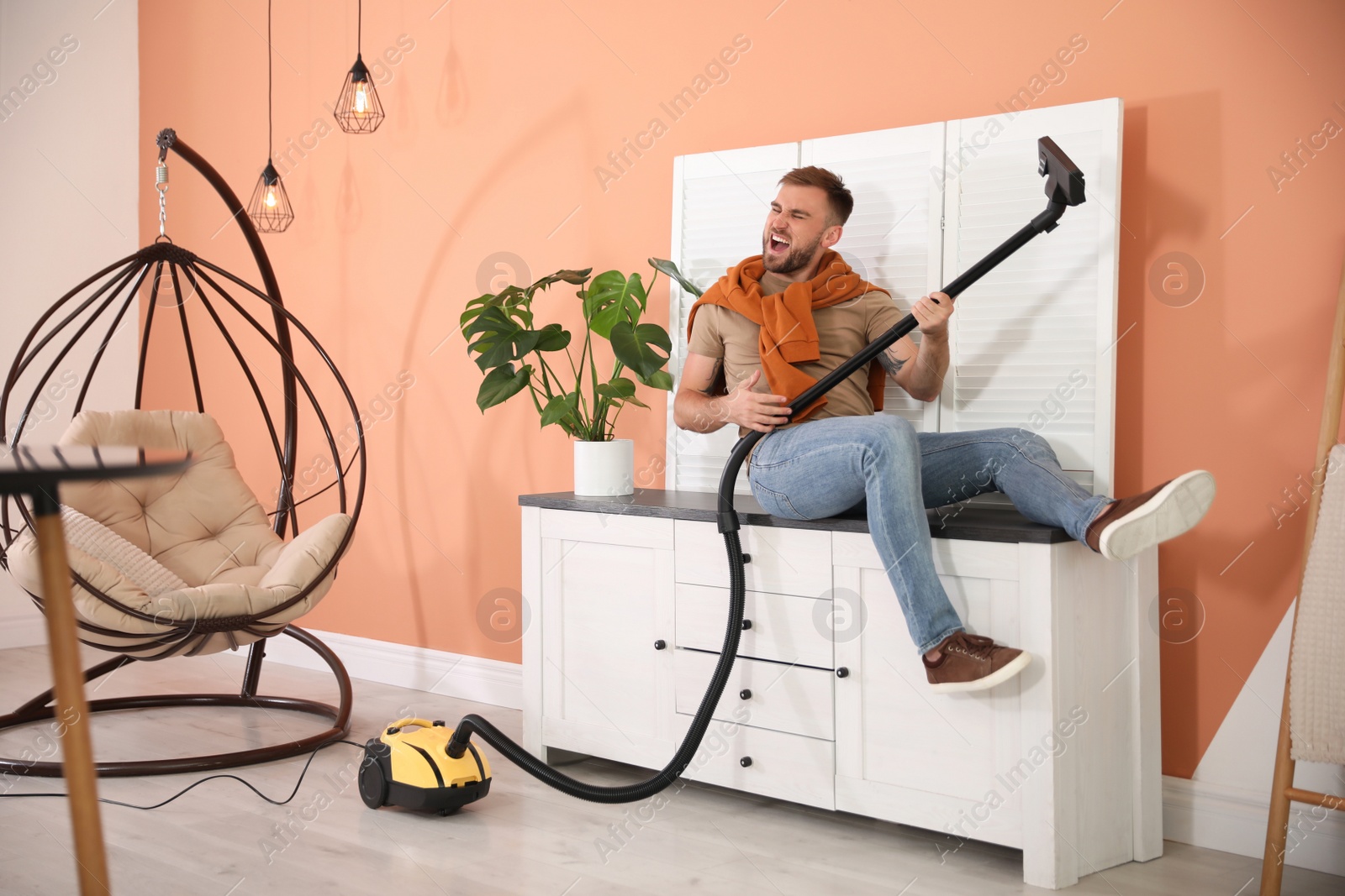 Photo of Young man having fun while vacuuming at home