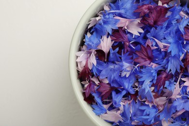 Photo of Beautiful colorful cornflowers petals in bowl on white table, top view. Space for text