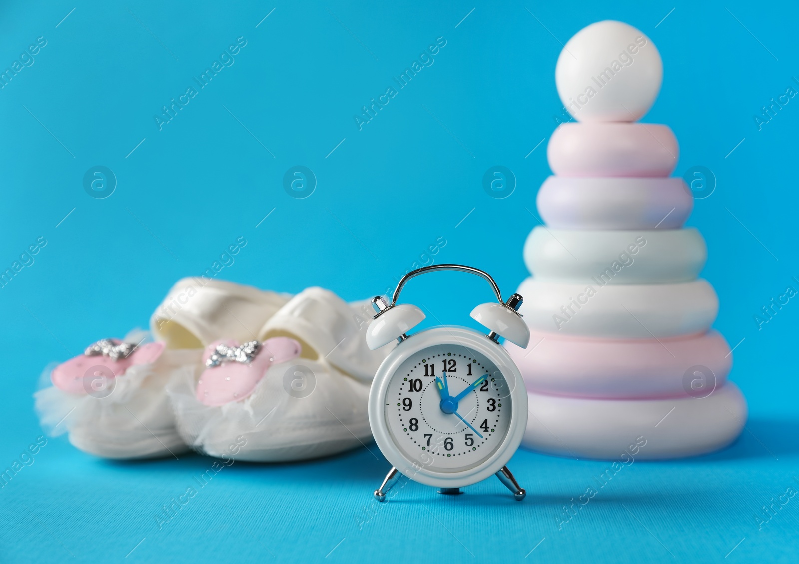 Photo of Alarm clock, toy pyramid and baby booties on light blue background. Time to give birth