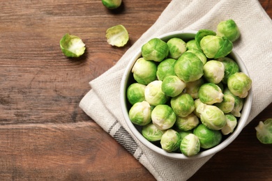 Bowl of fresh Brussels sprouts and napkin on wooden background, top view with space for text