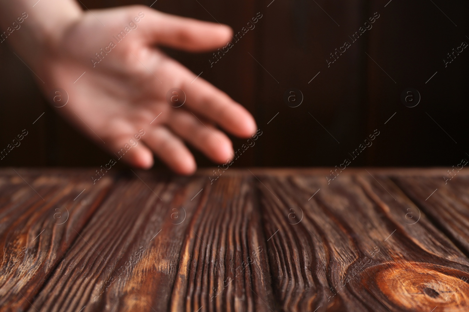 Photo of Woman holding hand above wooden table, selective focus. Space for text