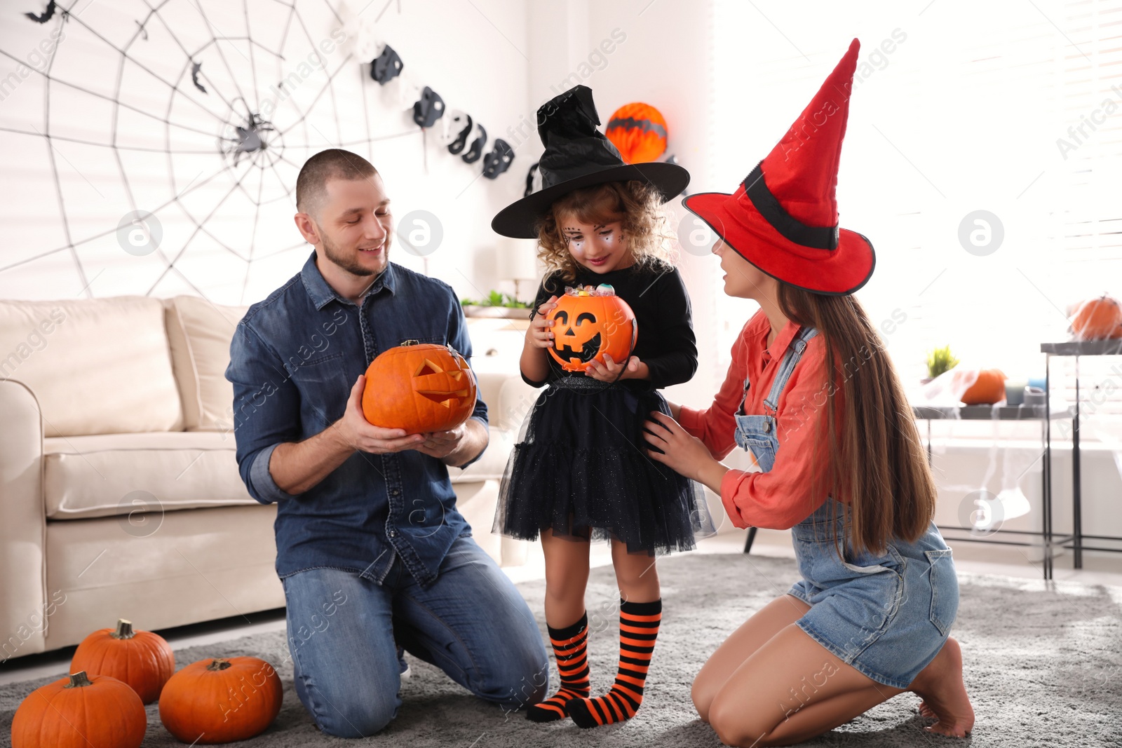 Photo of Parents and cute little girl with pumpkin candy bucket at Halloween party indoors