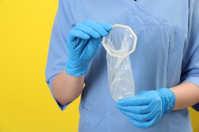 Photo of Doctor with unrolled female condom on yellow background, closeup. Safe sex