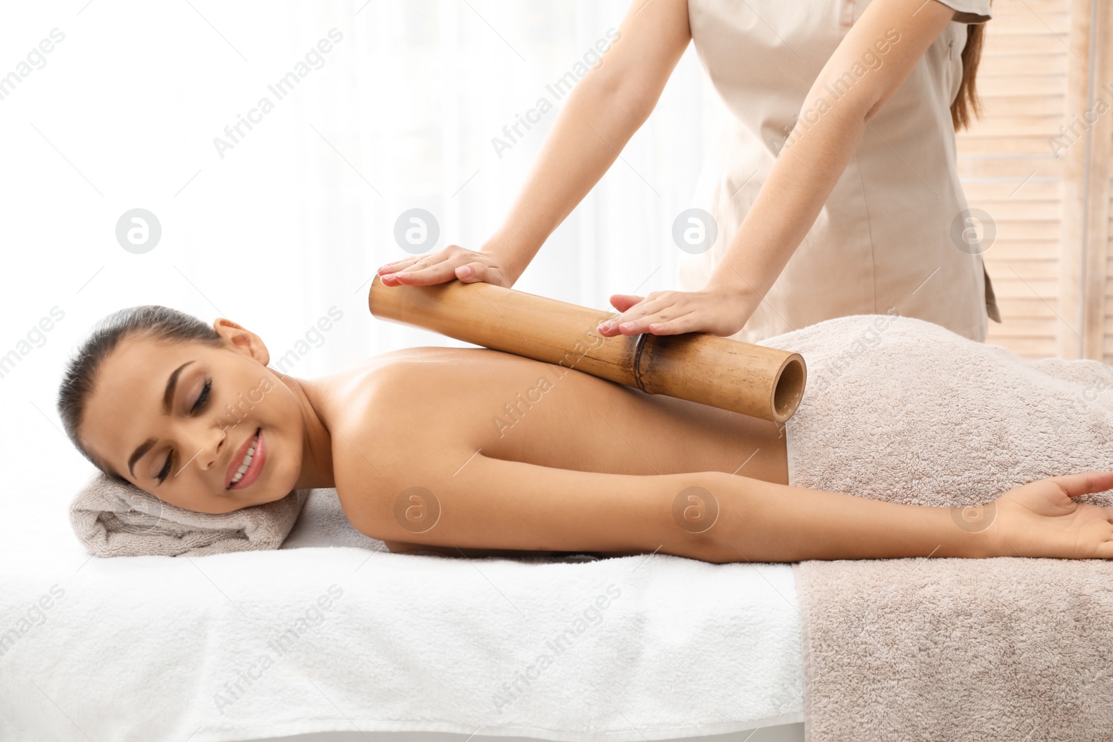 Photo of Young woman having massage with bamboo stick in wellness center