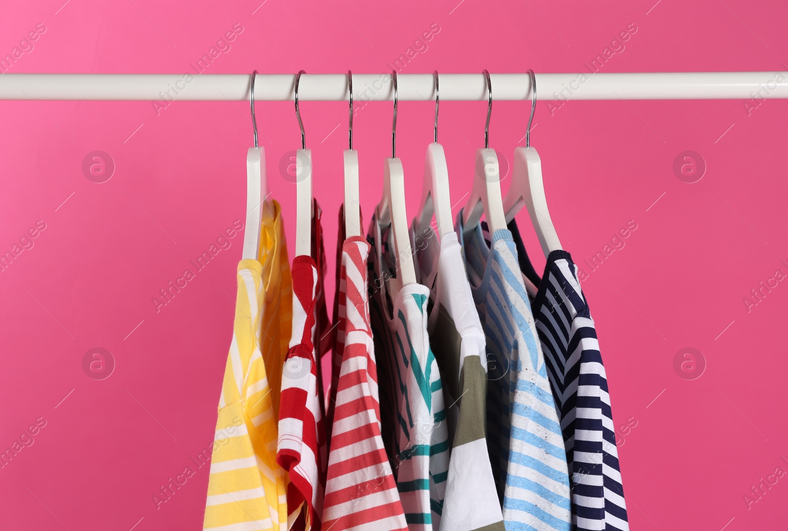 Photo of Colorful clothes hanging on rack against pink background