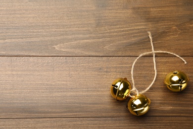 Golden sleigh bells with rope on wooden background, flat lay. Space for text