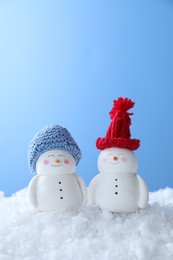 Photo of Cute decorative snowmen on artificial snow against light blue background