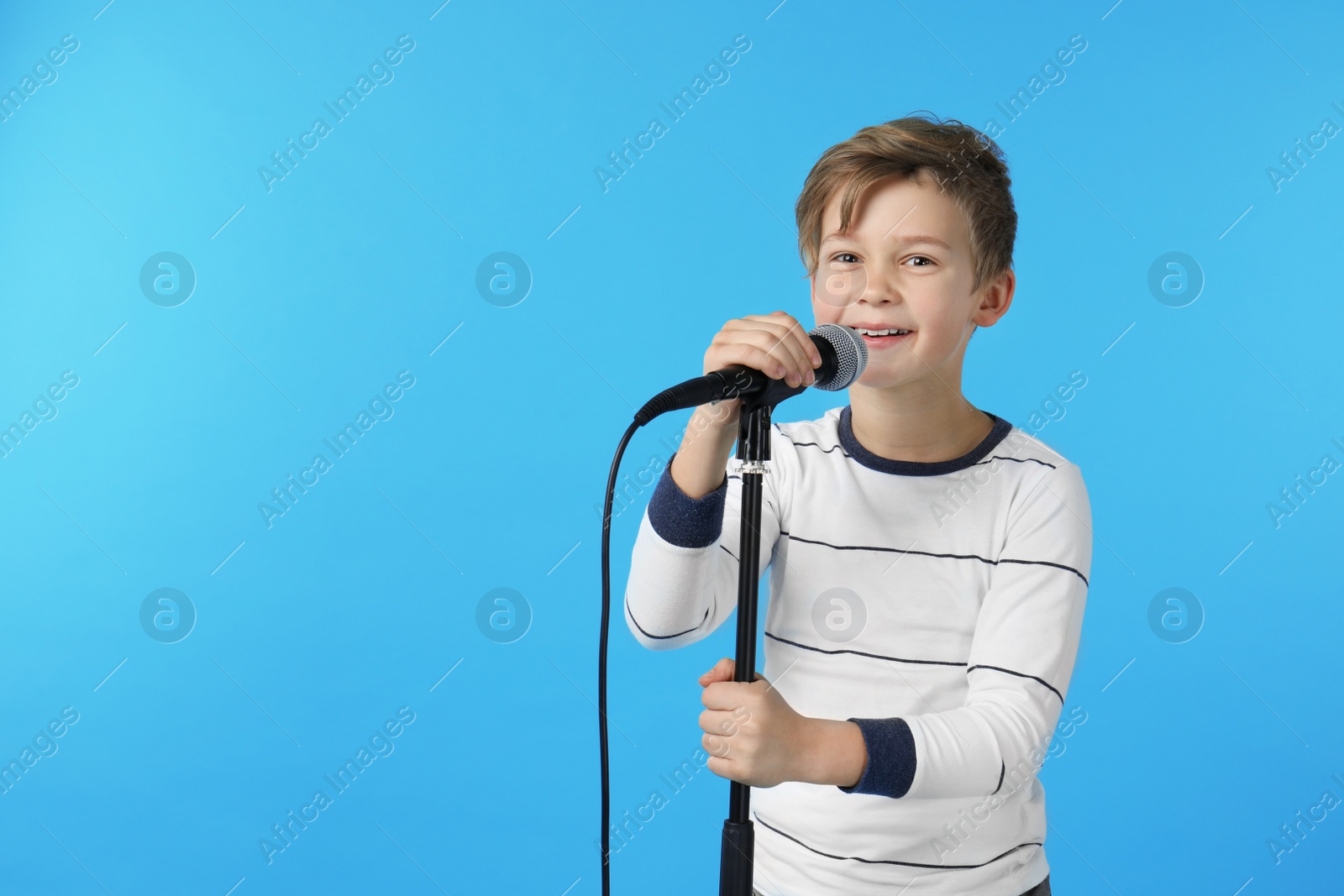 Photo of Cute boy with microphone on color background. Space for text