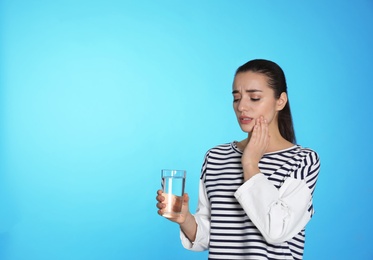 Photo of Emotional young woman with sensitive teeth and glass of water on color background. Space for text