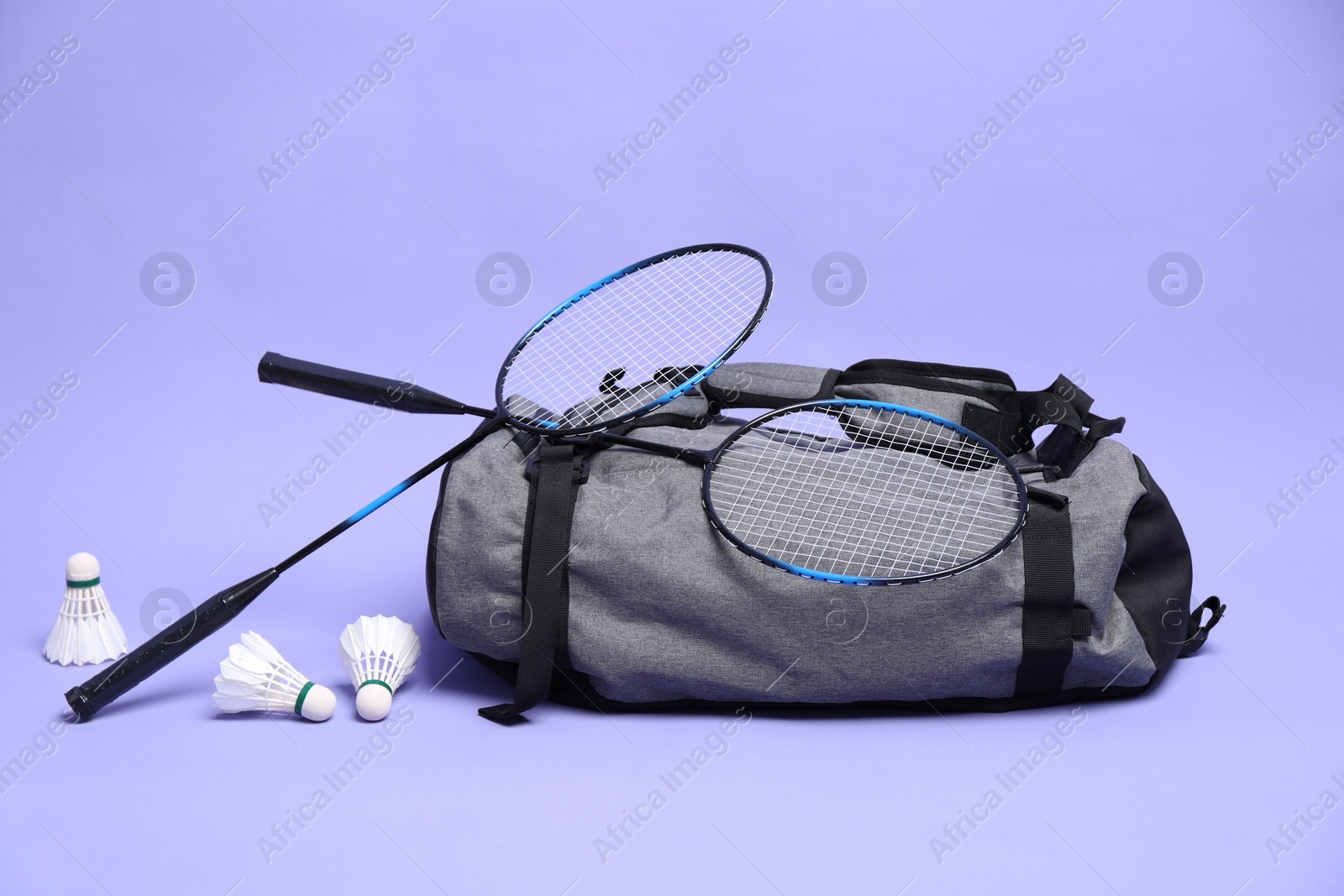 Photo of Feather badminton shuttlecocks, rackets and bag on violet background