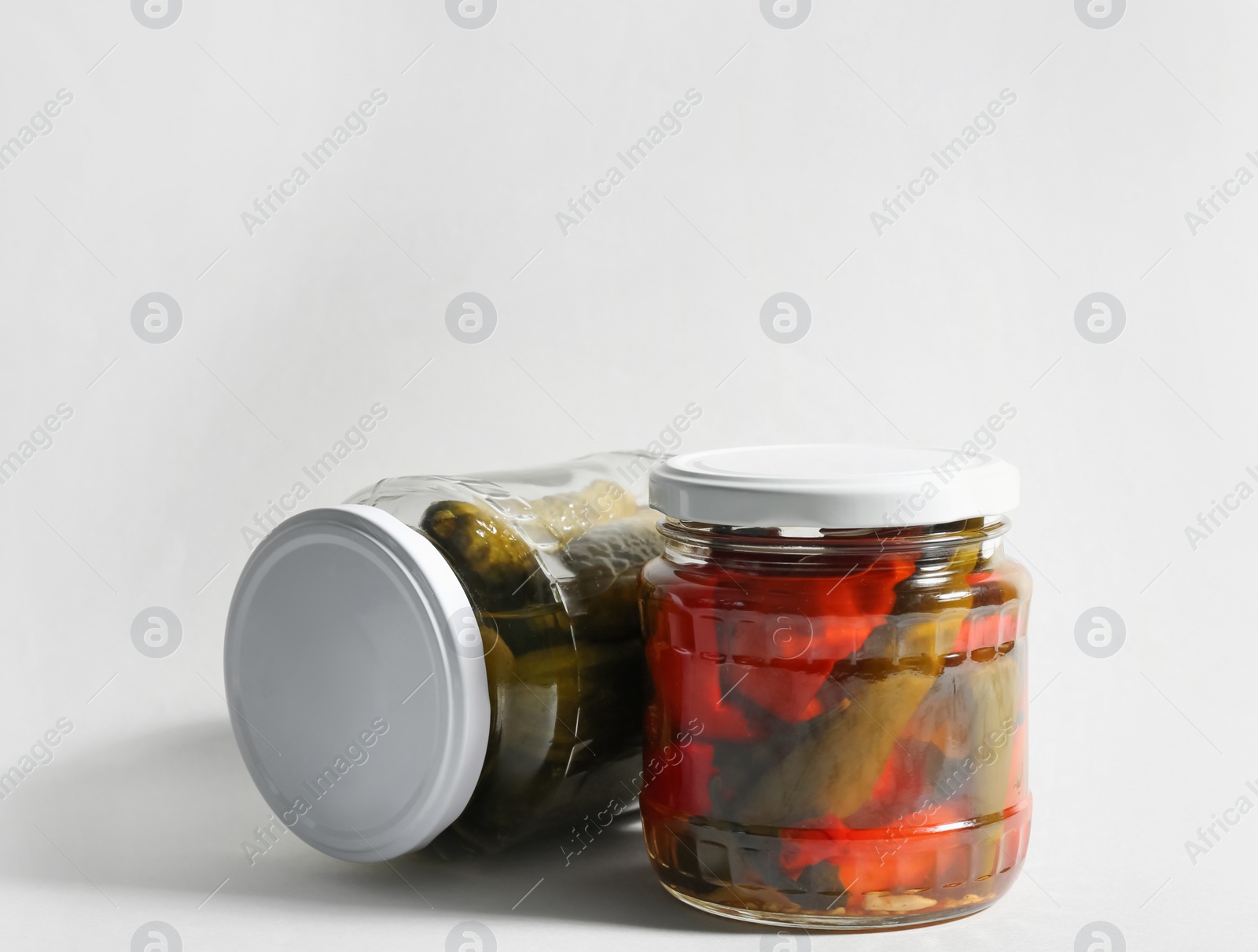 Photo of Glass jars with pickled bell peppers and cucumbers on white background