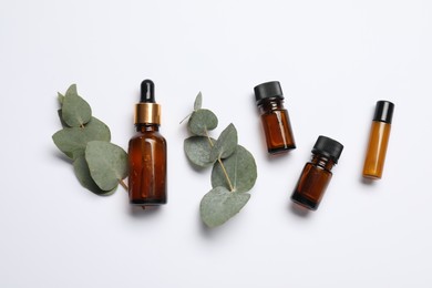 Photo of Aromatherapy. Bottles of essential oil and eucalyptus leaves on white background, flat lay