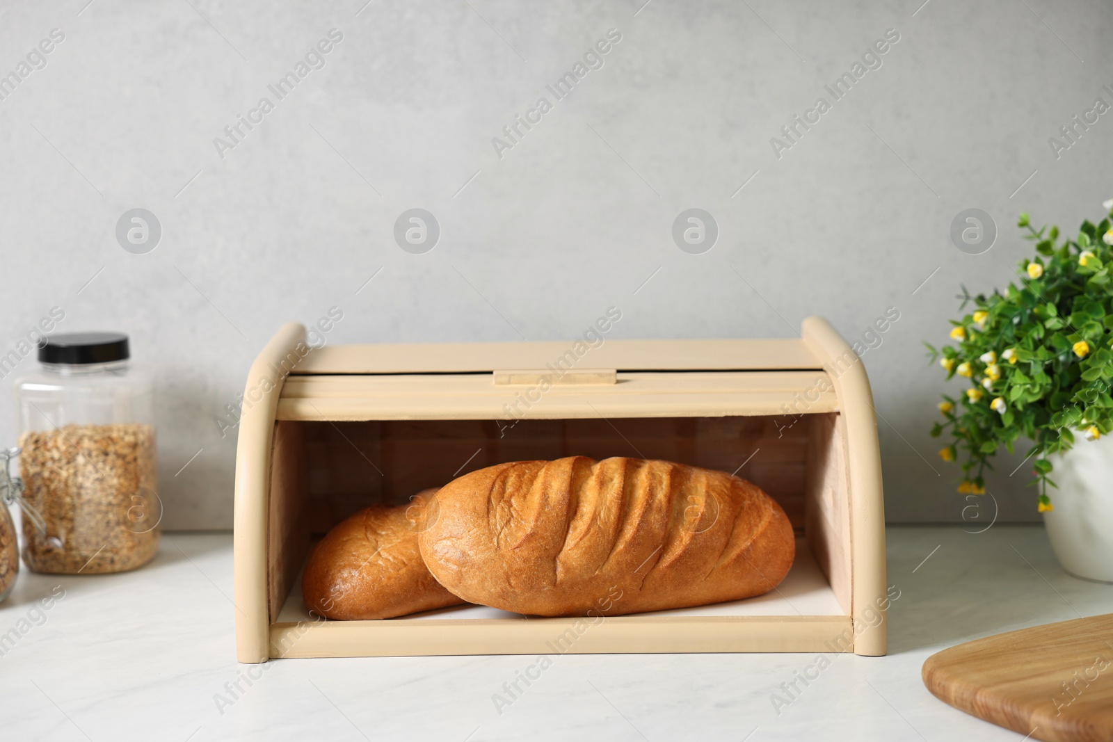 Photo of Wooden bread basket with freshly baked loaves on white marble table in kitchen