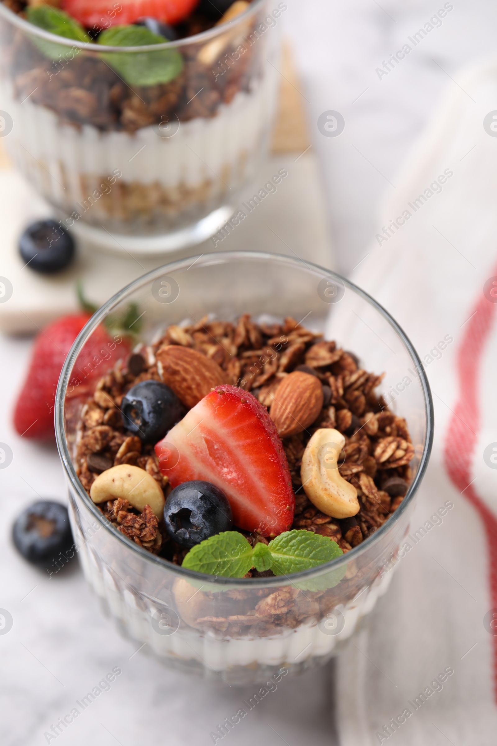 Photo of Tasty granola with berries, nuts and mint in glass on table, closeup