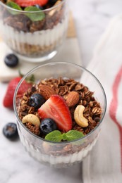 Photo of Tasty granola with berries, nuts and mint in glass on table, closeup