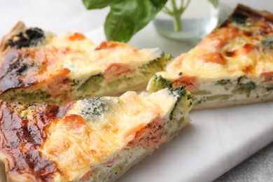 Photo of Pieces of delicious homemade quiche with salmon and broccoli on white board, closeup