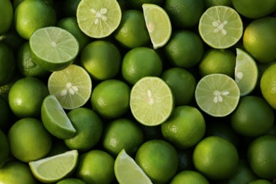 Photo of Whole and cut fresh ripe green limes as background, top view