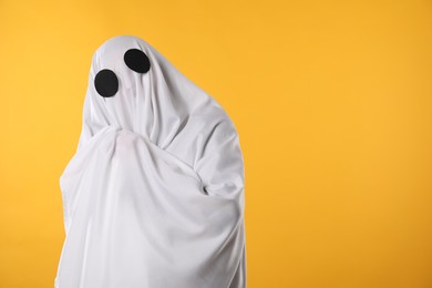 Creepy ghost. Person covered with white sheet on yellow background, space for text