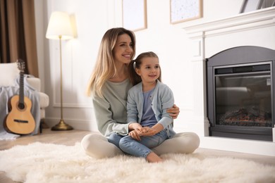 Happy woman with her daughter resting near fireplace at home