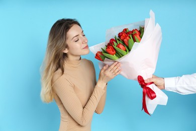 Photo of Happy woman receiving red tulip bouquet from man on light blue background. 8th of March celebration