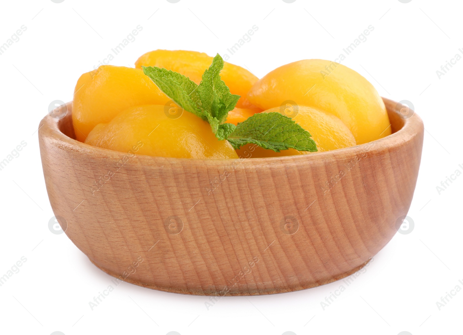 Photo of Halves of canned peaches with mint leaves in wooden bowl isolated on white