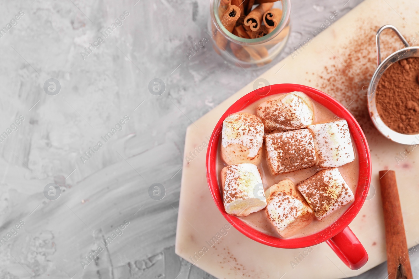 Photo of Cup of aromatic hot chocolate with marshmallows, cocoa powder and cinnamon sticks on gray table, flat lay. Space for text