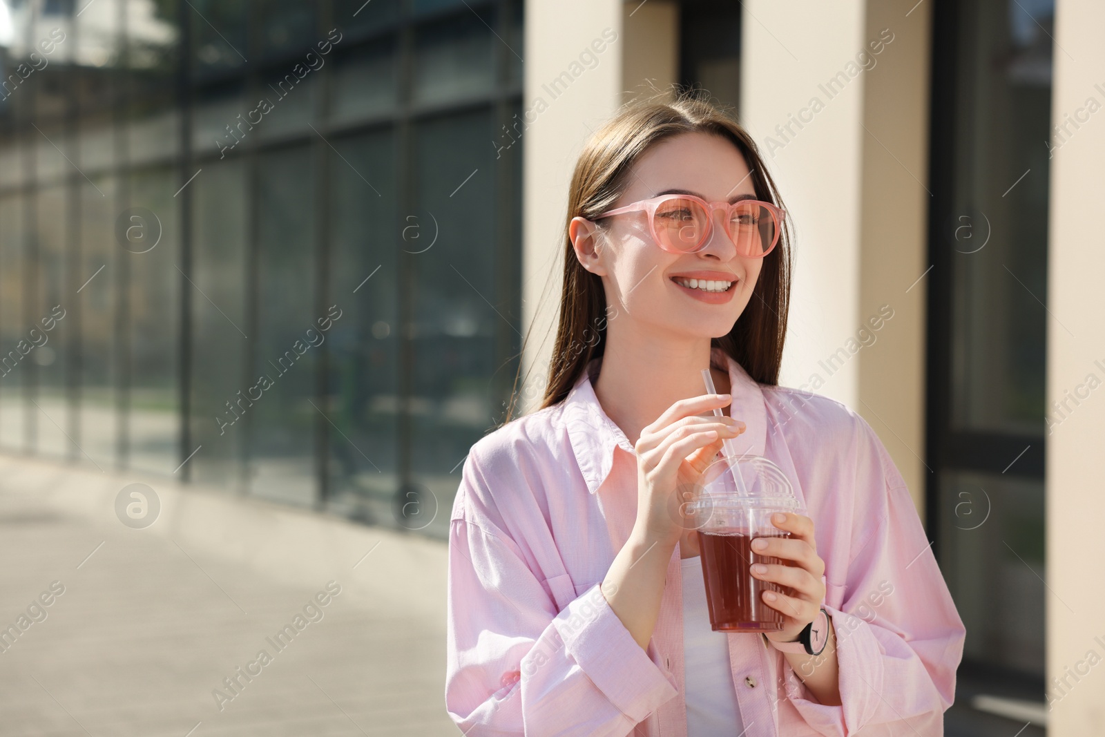 Photo of Young woman in sunglasses with plastic cup of fresh juice outdoors, space for text