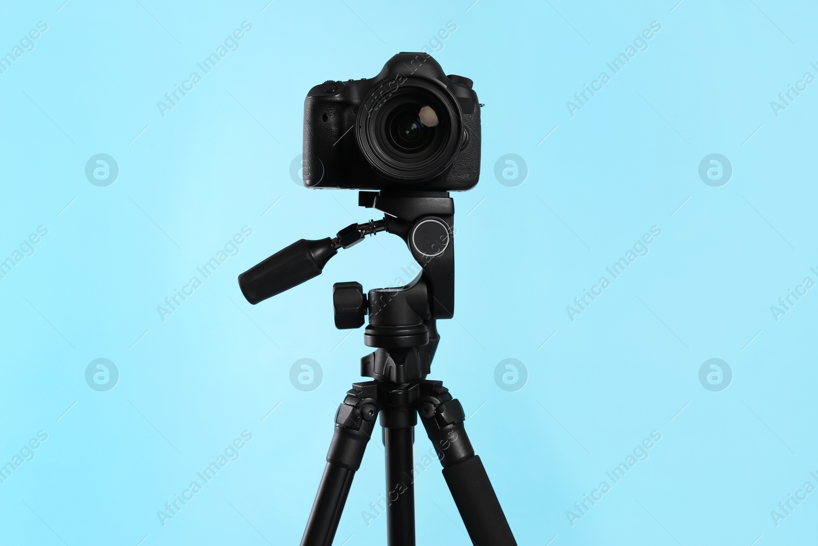 Photo of Modern tripod with professional camera on light blue background