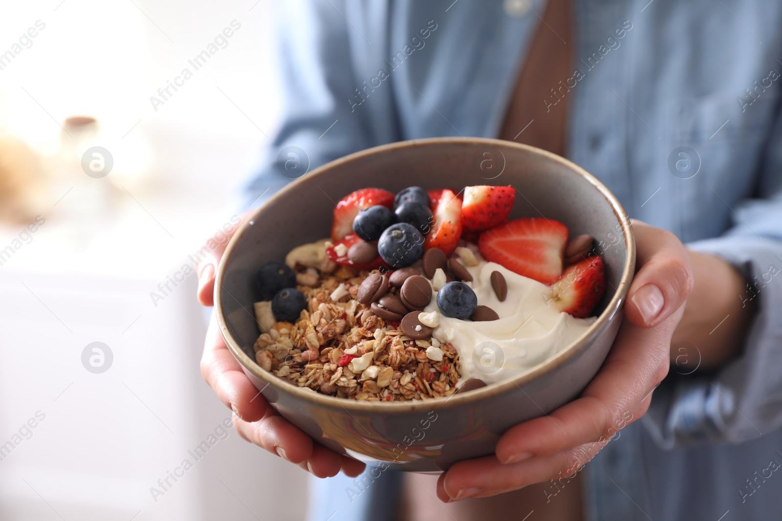 Photo of Woman holding bowl of tasty granola on blurred background, closeup