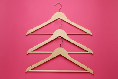Photo of Empty wooden hangers on pink background, flat lay