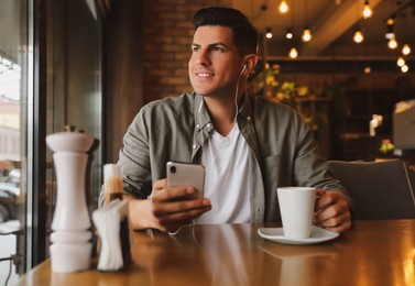 Man with smartphone listening to audiobook at table in cafe