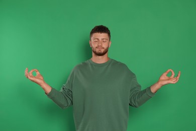 Photo of Young man meditating on green background. Zen concept