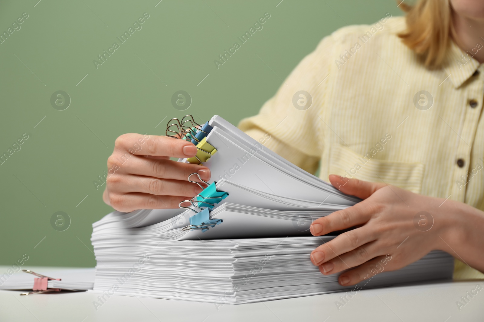 Photo of Woman stacking documents at white table against green background, closeup