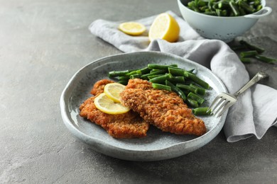 Tasty schnitzels served with lemon and green beans on grey table, closeup