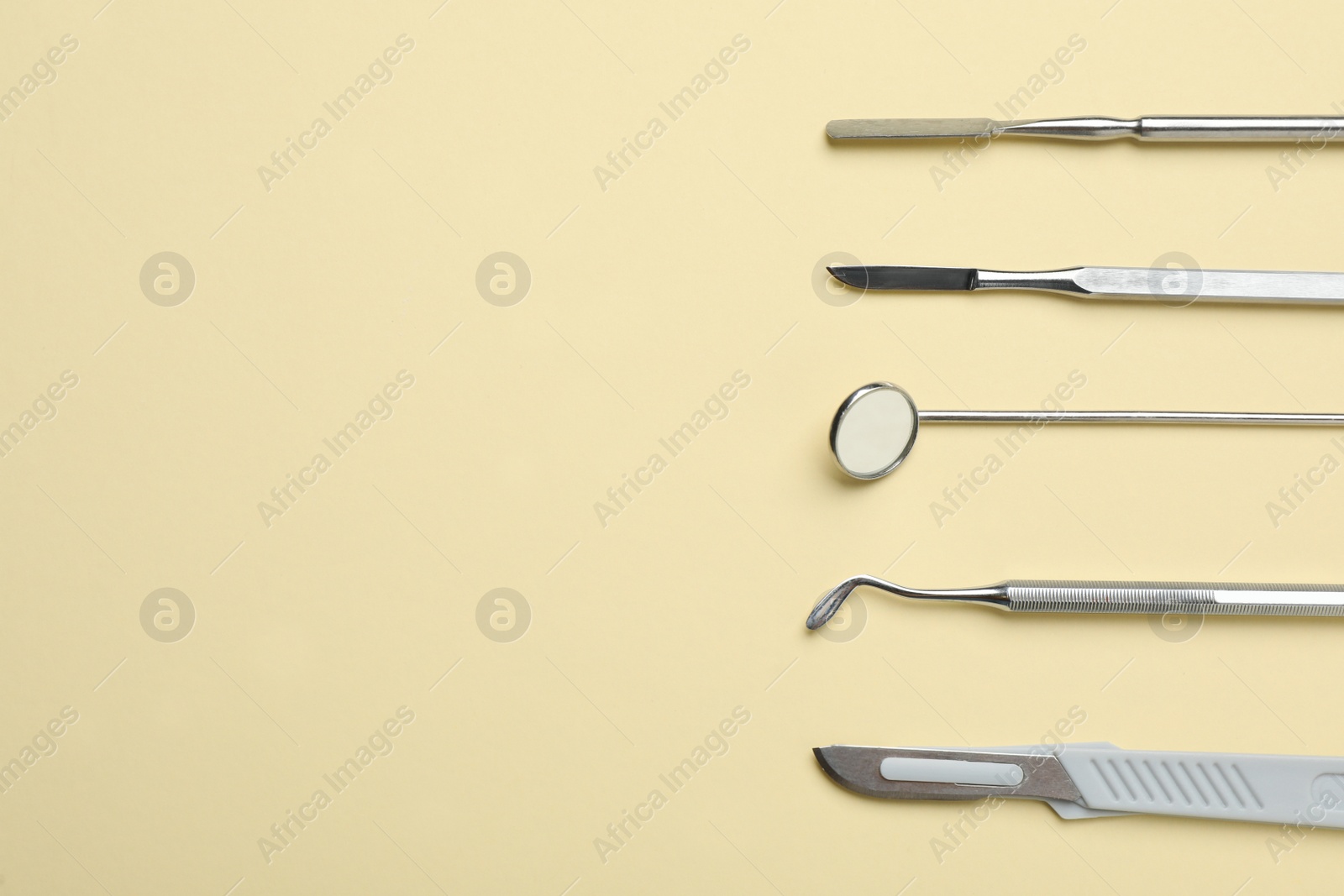 Photo of Set of different dentist's tools on pale yellow background, flat lay. Space for text