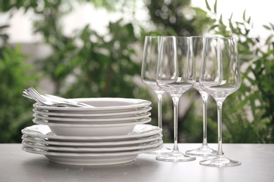 Photo of Set of clean dishware, cutlery and wineglasses on grey table against blurred background