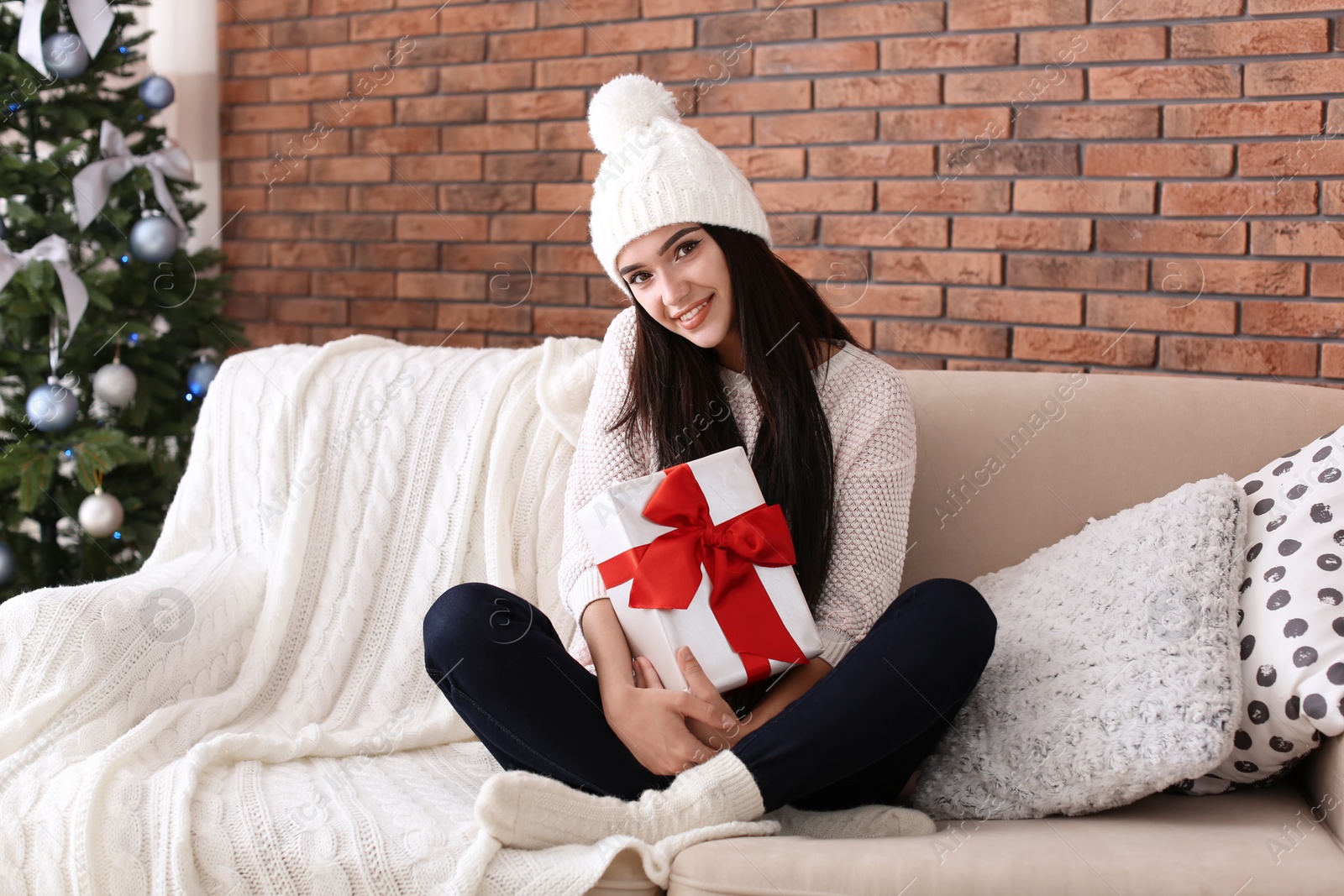 Photo of Beautiful young woman in hat with gift box at home. Christmas celebration