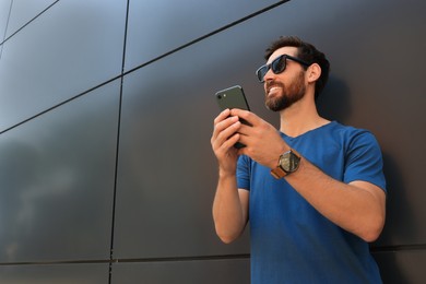Photo of Happy man with smartphone near grey wall. Space for text