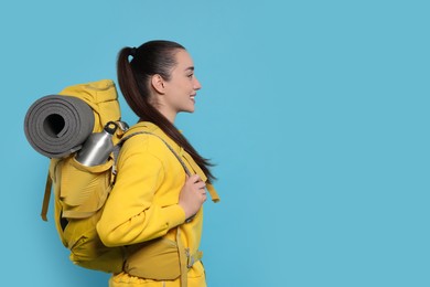 Smiling young woman with backpack on light blue background, space for text. Active tourism