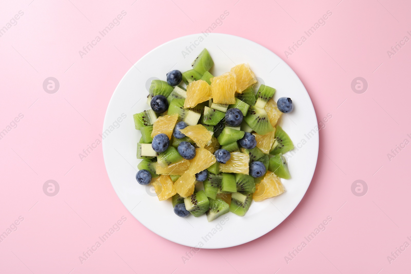 Photo of Plate of tasty fruit salad on pink background, top view