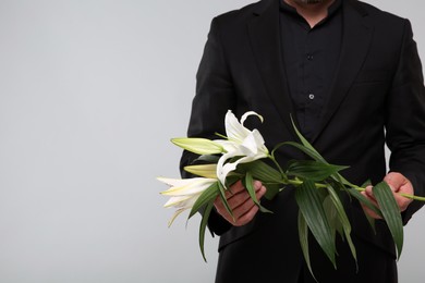 Photo of Man with white lilies on light grey background, closeup and space for text. Funeral ceremony