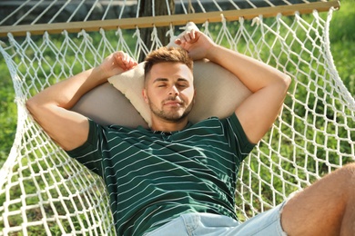 Young man resting in comfortable hammock at green garden